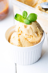 Homemade ice cream with salted caramel in a bowl on a white wooden background, soft focus, vertical