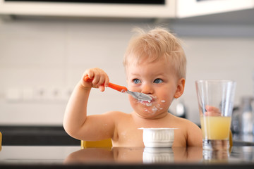 Adorable one year old baby boy eating yoghurt with spoon