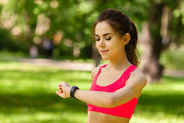 The woman is engaged in fitness in Park and looks at fitness tracker
