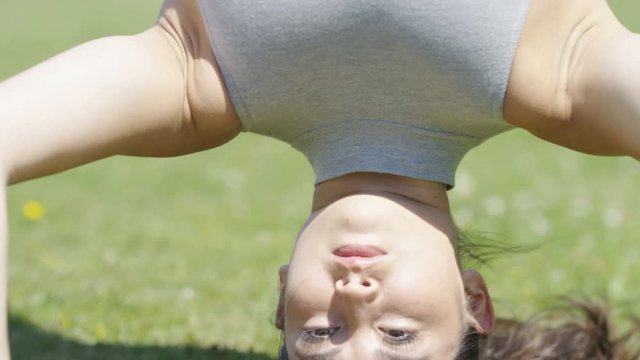 Young woman doing a yoga headstand outdoors, in slow motion