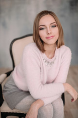 Fototapeta premium Soft photo of fresh young woman in pink tender sweater smiling. Pretty girl enjoying early sunny morning at home.