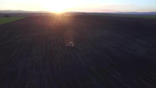 Drone flying over the tractor plowing against the sun