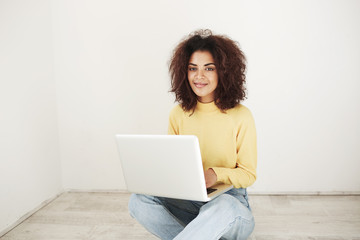 Cheerful beautiful african girl smiling looking at camera sitting with laptop on floor. Copy space.