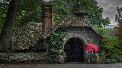 Woman sitting under a red umbrella on a rainy day in front of the old stone pump house at the New Jersey Botanical Gardens in Ringwood, NJ