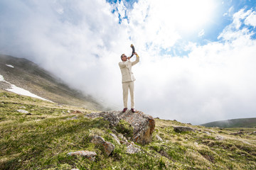 Businessman in a white suit blowing in the horn in the mountains