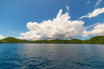 Rocky coastline of island spotted by islets and covered by dense lush green jungle in the colorful...