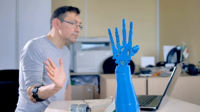 An engineer tests a blue robotic hand.