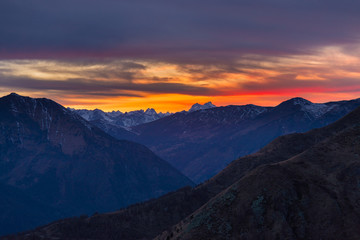 Naklejka na ściany i meble Colorful sunset behind majestic mountain peaks of the Italian Alps. Fog and mist covering the valleys below, autumnal landscape, cold feeling.