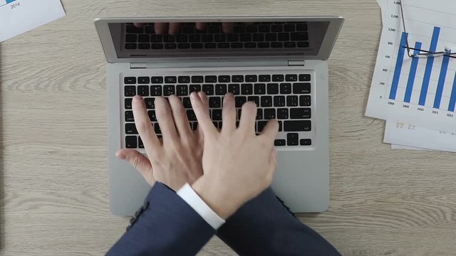 Two office workers typing on laptop actively, businessmen having fun at work