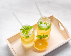 lemonade with fresh lemon and twig mint with drinking straw on wooden tray