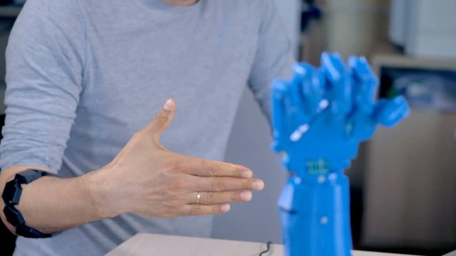 An engineer wearing armband controller gives directions to a robotic hand.