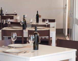 Tables set for lunch or dinner. Bottles of wine are present.