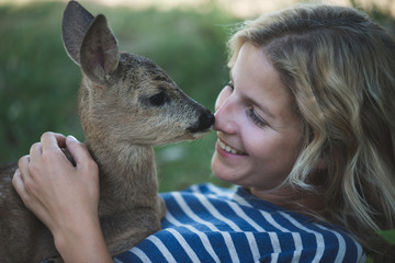 Cute blonde woman playing with roe deer fawn.