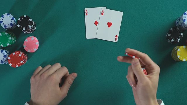 Man's hand holding poker chips, pair of aces cards, male thinking about bet