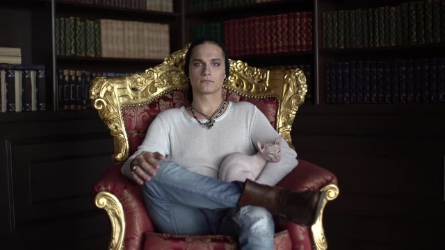 Strange man sitting on a throne in the library and holds Sphynx cat