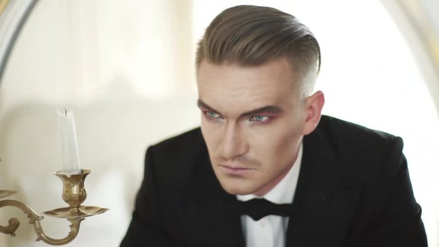 Reflection face in the mirror. Scary man in a tuxedo and bow tie looking in the mirror. Actor with makeup before going out to the theater stage. Actor plays of bad person