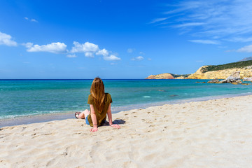 Fototapeta na wymiar Young woman sitting on beautiful sandy Firiplaka beach. South shore of the island of Milos. Cyclades Islands, Greece.