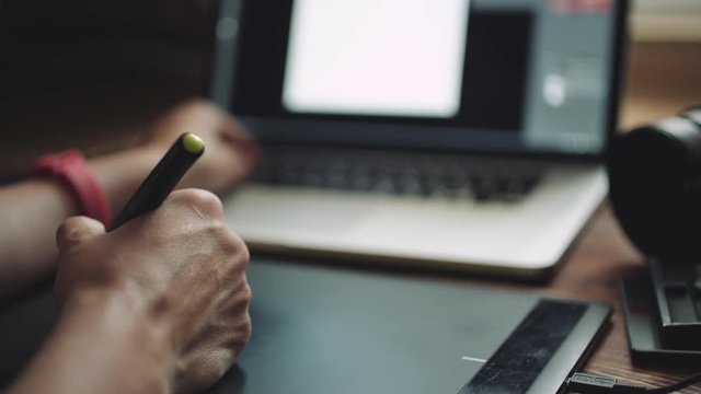Woman designer working at a laptop with a graphics tablet. Close-up, sliding shot