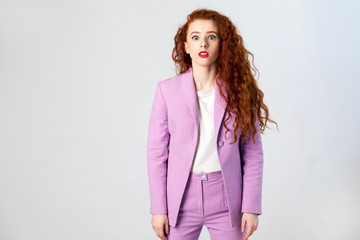 Portrait of surprised beautiful business woman with red - brown hair and makeup in pink suit. looking at camera, studio shot on gray background.