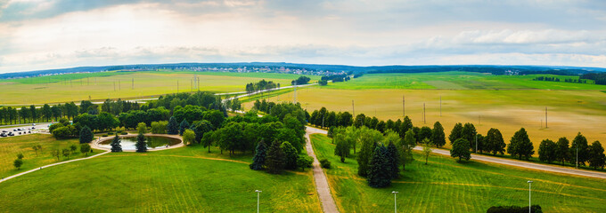 Obraz premium Panoramic rural area. Green fields, meadows, trees, pond, roads and sky with clouds. Minsk region Belarus.