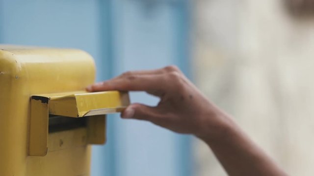 Woman is sending a blue letter into a yellow letterbox. Slow motion 120 fps