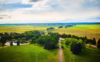 Obraz premium Green countryside landscape. Fields, meadows, trees, pond, roads, houses on the horizon and sky with clouds. Minsk region, Belarus