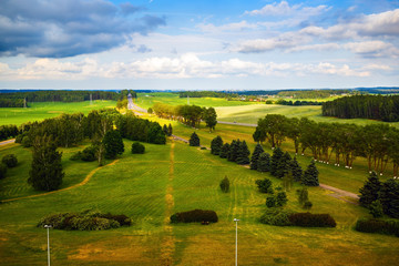 Fototapeta na wymiar Green fields, meadows, trees, road and blue sky with clouds. Bright summer landscape. Minsk region, Belarus