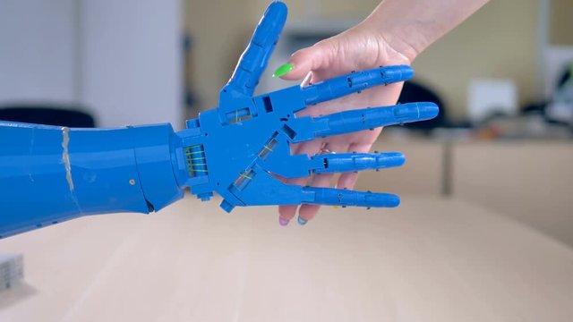 A bionic hands greets a female one by shaking.