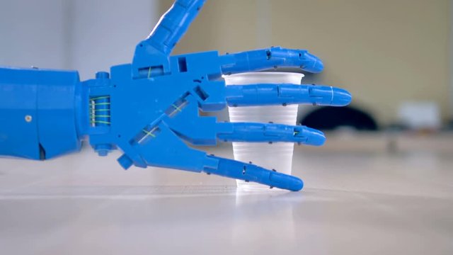 A bionic hand grabs a plastic cup.
