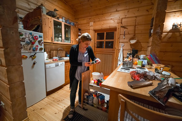 Woman standing in kitchen of  log cabin looking at food, Iceland, Europe.