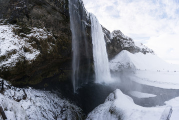 Tourists viewing snow covered landscape and high waterfall, Iceland, Europe.
