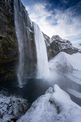 Tourists viewing snow covered landscape and high waterfall, Iceland, Europe.