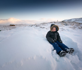 Fototapeta na wymiar Young boy sitting in deep snow covered landscape, Iceland, Europe.