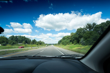 View of main road seen through car windscreen with white clouds in sky.