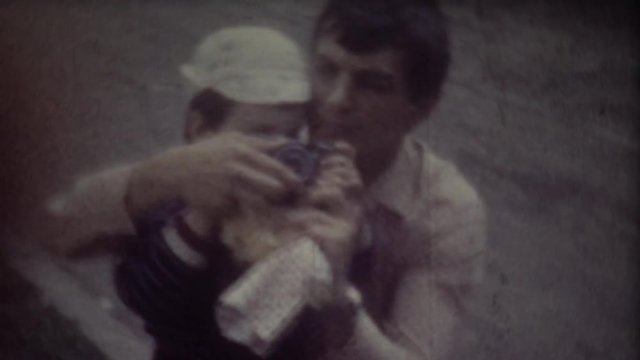 Father teaches son to photographing. Screenshot of 8mm retro camera. Family video archive.