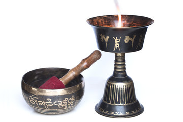 Tibetan buddhist lit oil lamp with singing bowl close up. Burning fire. Black metal with golden...