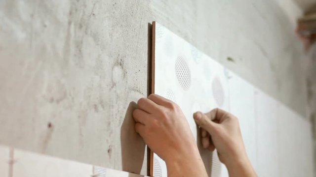 Unrecognizable ceramist is laying tiles on bathroom wall. Slow motion