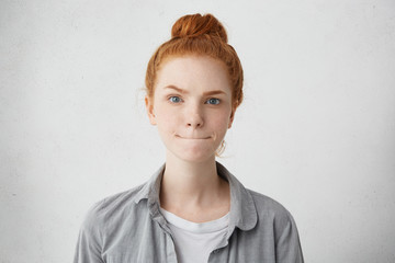 Cute ginger female with warm alluring blue eyes wearing gray shirt pressing her lips and raising eyebrows thinking over her future plans in life. People, body language, lifestyle, facial expressions