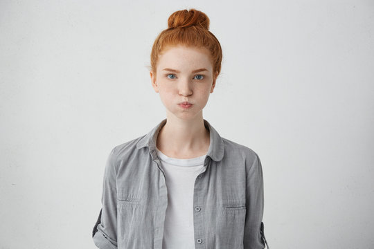 Portrait of grumpy woman with freckled face, blue eyes, ginger hair and eyebrows blowing her cheeks being dissatisfied with her results. Pretty red-haired girl making grimace having upset look