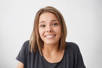 Magnificent pretty woman with dark narrow eyes and pleasant smile shrugging her shoulders having nice and doubtful look while posing against white background. Impressive female with beautiful face