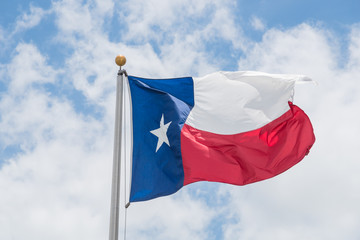 Large Texas (The Lone Star) flag waving on flag pole with cloud blue sky. Windy and sunny day with waving flag blowing/flowing. Ruffled Texas flag. Room for text, copy space.