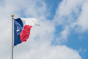 Large Texas (The Lone Star) flag waving on flag pole with cloud blue sky. Windy and sunny day with...