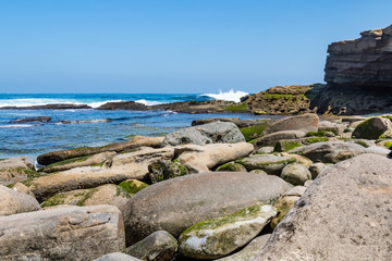 Fototapeta na wymiar Ocean waves crash onto boulders strewn upon the beach at La Jolla Cove in San Diego, California. 