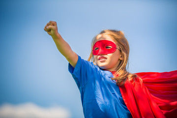 Naklejka premium Funny little girl playing power super hero over blue sky background. Superhero concept.