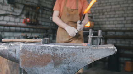 Close up view - hands of Blacksmith with gloves in forge makes steel knife