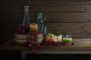 Fresh fruits in the rattan basket and bottle with glass on the plank in room it dim light / Still Life Image and selective focus..
