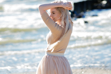 Young cheerful girl on the seashore. Young blonde woman smiling. Trendy beige skirt