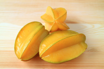 Three vivid yellow ripe whole fruits Star Fruit on natural wooden table