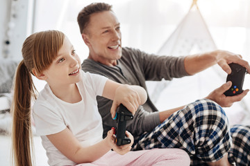 Obraz na płótnie Canvas Engaged emotional child and her father using controllers for playing