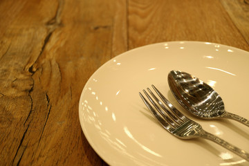 Off White Ceramic Plate with Silver Spoon and Fork on the Wooden Table 